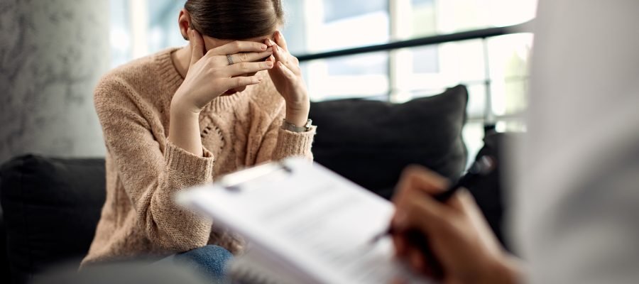 Depressed woman having psychotherapy session at doctor’s office. Sad woman holding her head in pain while having a meeting with psychotherapist.